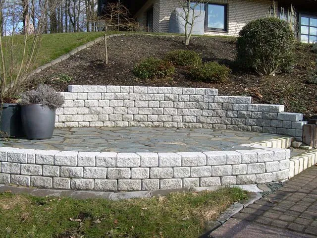 Halbkreisförmige Natursteinsitzmauer mit Bepflanzung im Privatgarten