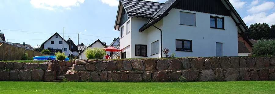 Panoramaansicht: Wohnhaus mit eingefriedeter Sandsteinmauer und ebener Rasenfläche